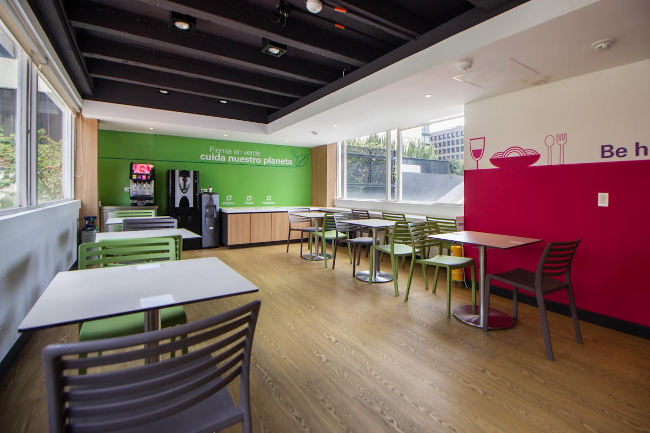 gallery-02 Spacious cafeteria with a minimalist design, featuring colorful chairs and tables, ready for dining.